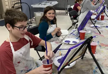 boy painting at table easle